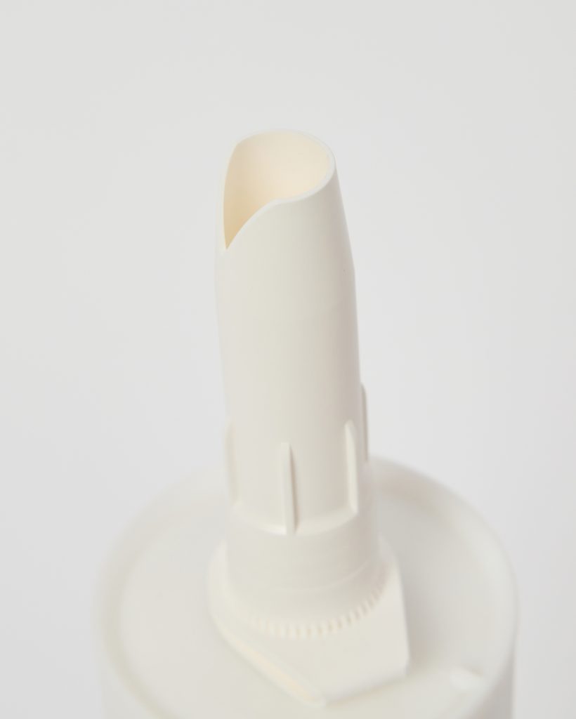 Close-up van een WoodUpp aanbrengmondstuk: witte kunststof spuitmond met schuine snijkant, geribbelde draaikraag en ronde basis van een WoodUpp tube/applicator. Minimalistische, matte finish, ontworpen voor nauwkeurig doseren van vulpasta of lijm bij houtreparaties, voor kleine naden en scheuren, gebruik in combinatie met WoodUpp reparatiesets en spuitmondverlengers.