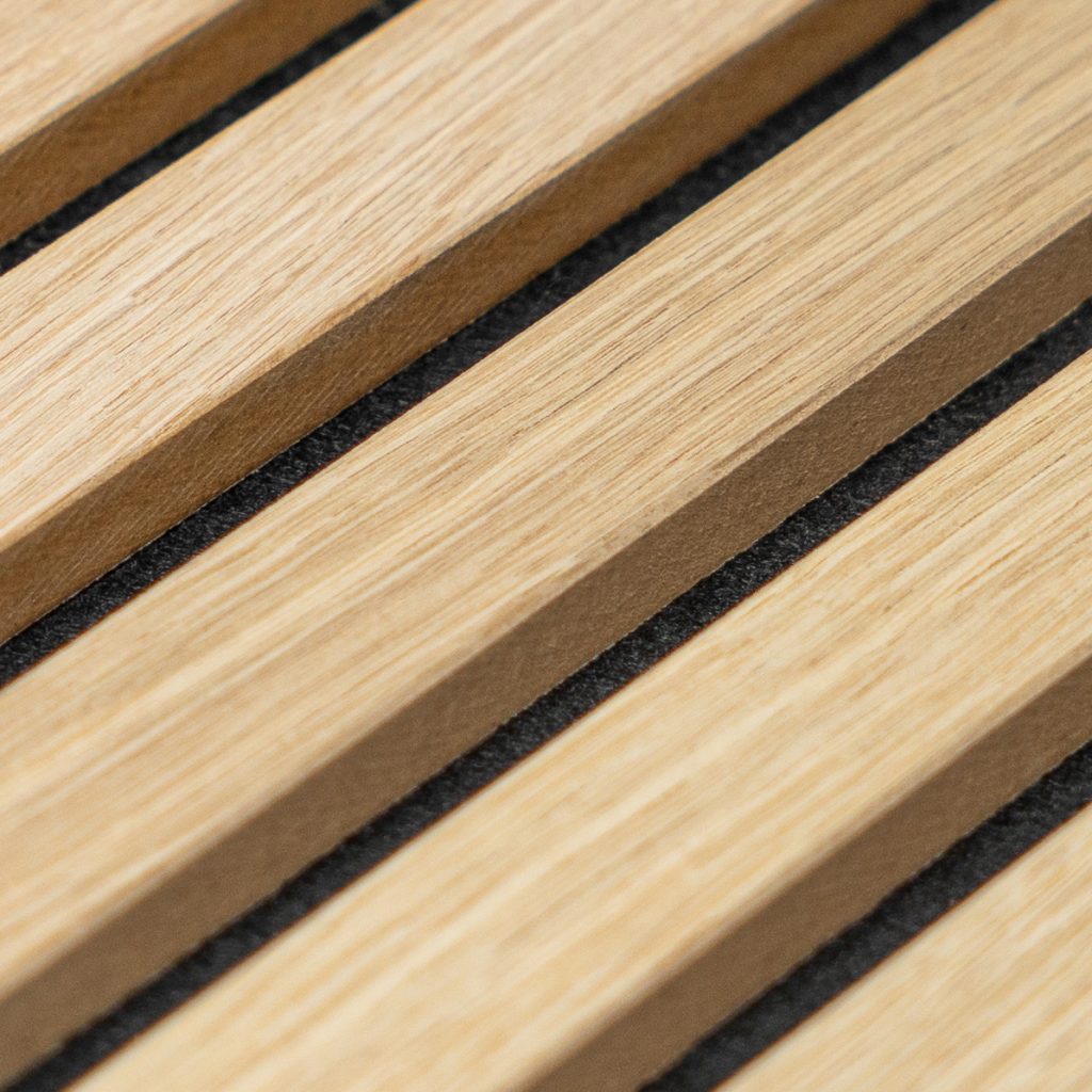Close-up van WoodUpp akoestische lamellenpaneel: licht eiken houten latten met fijne nerf, strakke diagonale rijen, zichtbare diepte en matte afwerking. Tussen de latten lopen smalle zwarte viltvoegen die contrast en geluidsabsorptie bieden, duurzaam en esthetisch, ideaal als wandpaneel voor moderne interieurs.