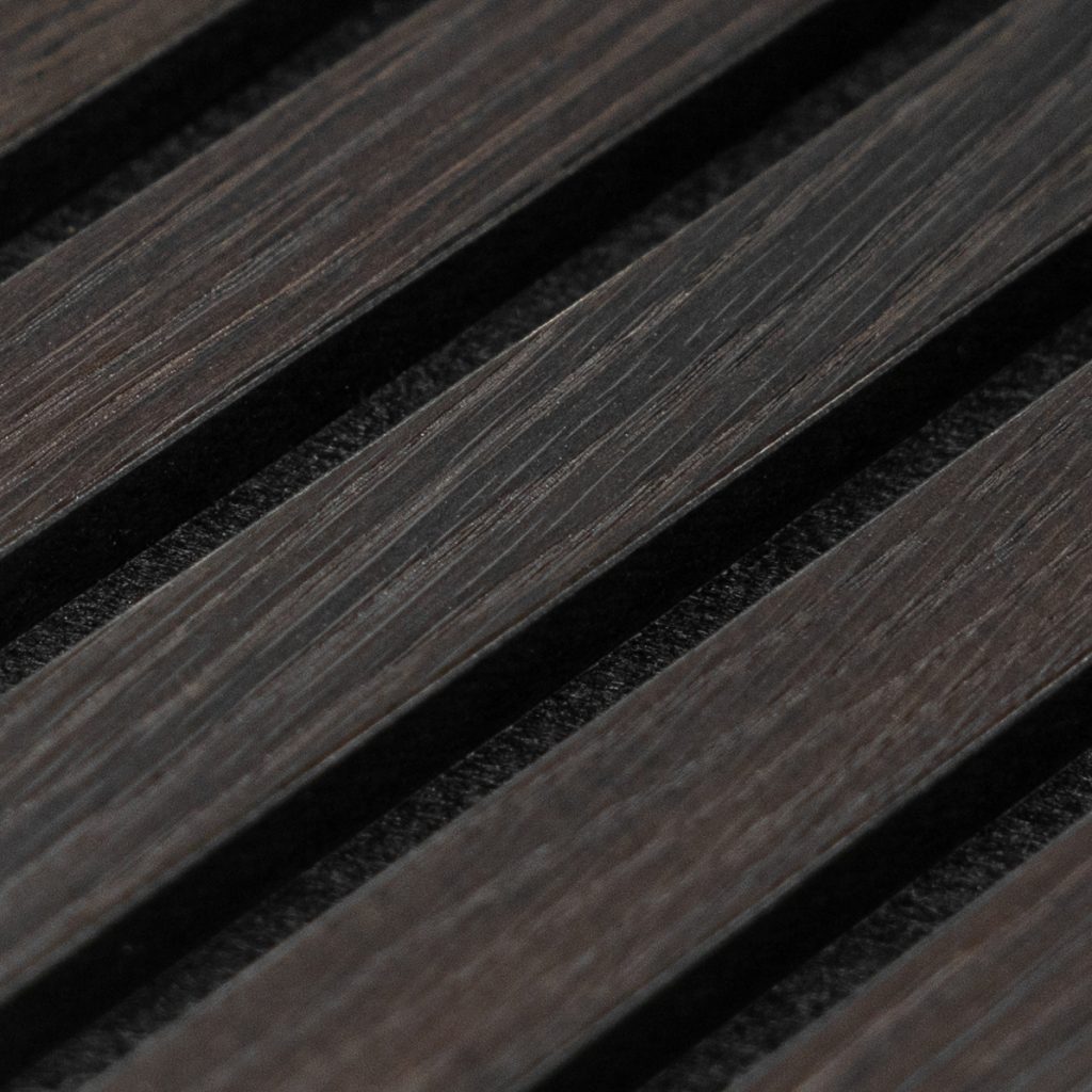 Close-up van WoodUpp slatpanelen: gelijkmatige, smalle donkerbruine houten latten met zichtbare nerf en matte afwerking, strak diagonaal geplaatst en gescheiden door diepe zwarte voegen met akoestische vulling. Met subtiele tintverschillen en nauwkeurig gefreesde randen, modern minimalistisch slat-design voor wanden en geluidsabsorptie.