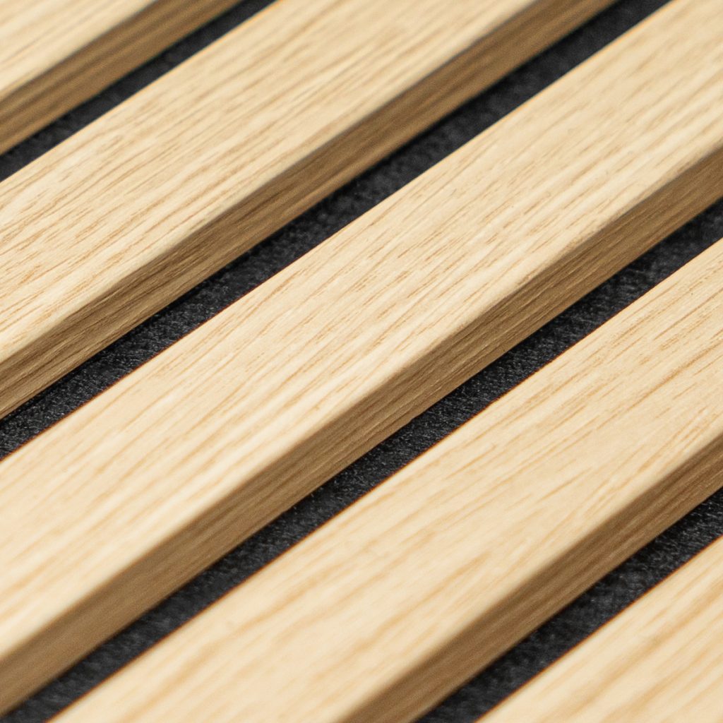 Close-up van WoodUpp slatpanelen: smalle, licht eikenhouten lamellen in diagonale rij, gemonteerd op een donkergrijze akoestische viltachtergrond. Duidelijke houtnerf en strakke voegen tonen de afwerking van WoodUpp's houten lamellen voor wand- en plafondbekleding, bedoeld voor esthetiek, hoogwaardige afwerking, geluidsabsorptie en subtiele schaduwwerking.