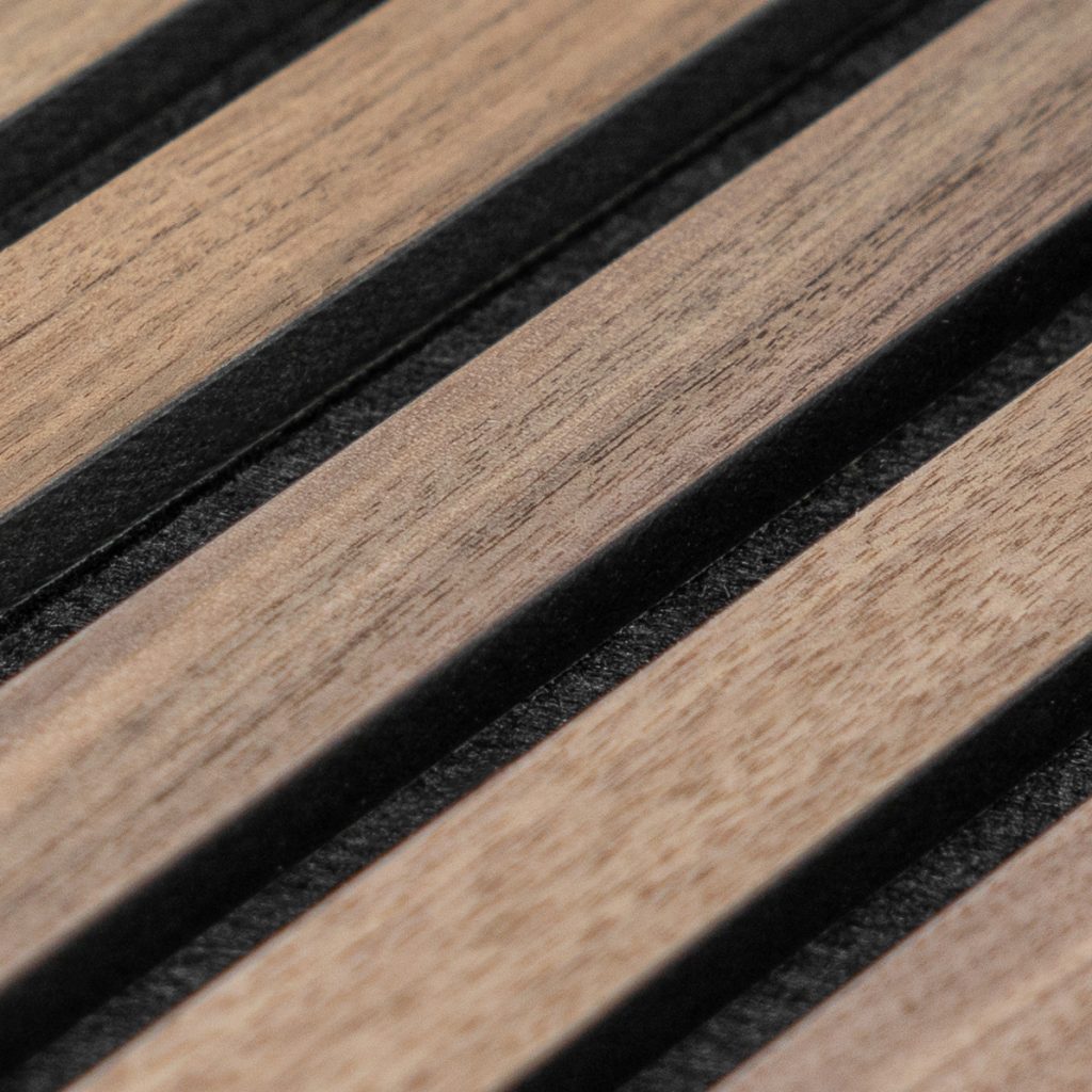 Close-up van WoodUpp lamellenpaneel: smalle, lichte houten latten met zichtbare nerf, afgewisseld met zwarte, diepere voegen. Het vlak toont een strak, ritmisch patroon van houten stroken op zwarte akoestische achtergrond, geschikt als decoratieve wand- of plafondbekleding van hoge kwaliteit en natuurlijke uitstraling.