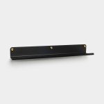 Zwarte smalle metalen wandplank van WoodUpp, matte afwerking en afgeronde rand. Platte display- en fotoplank met opstaand lipje om boeken, fotolijsten of decoratie te dragen. Drie goudkleurige schroeven zichtbaar als bevestiging, minimalistisch en modern ontwerp geschikt voor aan de muur.
