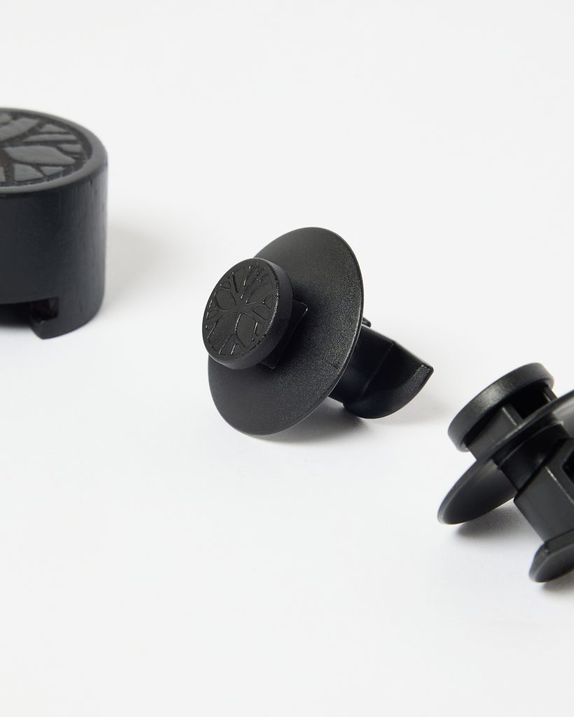 Close-up van drie zwarte WoodUpp-accessoires op witte achtergrond: twee kunststof ventilatieclips/airvent-adapters met brede ronde schilden en een losse ronde magneetadapter. Beide tonen het WoodUpp-boomlogo in reliëf; strakke matte afwerking, bedoeld om smartphones in autoventilatie te bevestigen en veilige, trillingsarme steun te bieden.