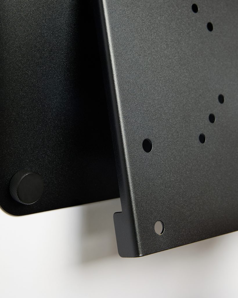 Close-up van twee zwarte, mat gecoate metalen bevestigingsplaten van WoodUpp, met meerdere ronde montagegaten, afgeronde randen en een ruwe, geribbelde bevestigingsknop. Het detail toont de textuur van de poedercoating, uitsparingen en kantelbevestiging voor monitorarm of accessoires in strak industrieel design en robuuste uitvoering.