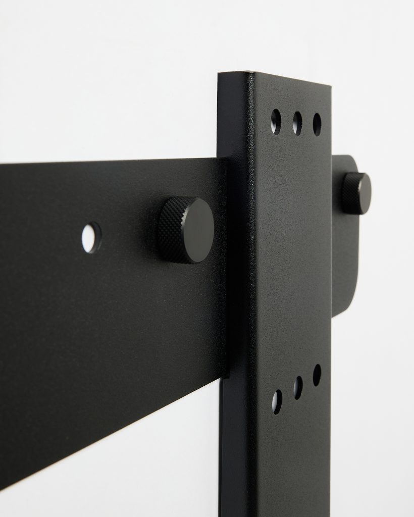 Close-up van een WoodUpp montagebeugel en bevestigingsknoppen: matzwart poedergecoate stalen verticale en horizontale platen met drie ronde montagegaten, twee geribbelde zwarte knopbouten, een klein doorboord bevestigingsgat, duidelijke coatingtextuur en fijne ribbelstructuur op de knoppen, close-up perspectief toont de precieze constructie.