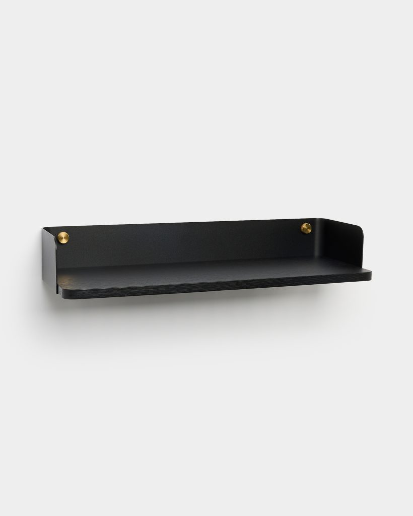 WoodUpp zwarte wandplank met matte metalen achterwand en zwarte houten plank, zwevend gemonteerd tegen een witte muur. De smalle, rechthoekige plank heeft opstaande zijkanten en twee zichtbare messing bevestigingsknoppen, met subtiele gouden accenten, een minimalistisch en functioneel design voor decoratie of opbergruimte.