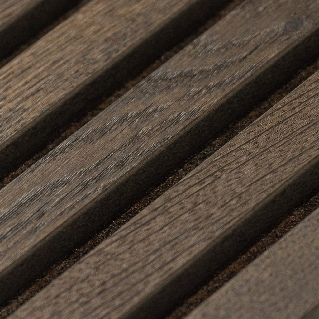 Close-up van een WoodUpp lamellenpaneel: donkerbruine, fijnnerfige houten latten met zichtbare nerf en matte afwerking, schuin geplaatste ribbels en gelijkmatige tussenruimtes gevuld met donkerbruin vilt die akoestische vulling suggereren, met subtiele kleurvariaties en een warme, natuurlijke uitstraling.