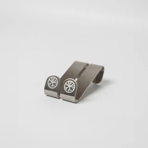 Close-up van twee WoodUpp geldclips: geborstelde roestvrijstalen, S‑vormige clips met afgeronde uiteinden. Op beide uiteinden staat het witte, cirkelvormige WoodUpp-logo (boom-/wielmotief). De minimalistische, compacte clips liggen naast elkaar op een neutrale witte achtergrond, strak, functioneel en hoogwaardig afgewerkt met subtiele lasergravure.