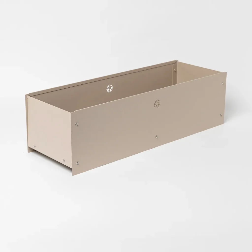 WoodUpp metalen plantenbak in beige: een langwerpige, rechthoekige bloembak met open bovenkant, strakke gepoedercoate zijwanden, zichtbare schroeven en kleine bloemvormige ventilatie-openingen in het voorpaneel en binnenzijde. Eenvoudig, modern ontwerp, geschikt voor planten en makkelijk te monteren.