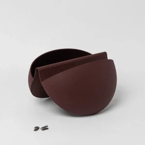 WoodUpp wandplantenbak in chocoladebruin: twee naadloos vormgegeven halve bolvormige modules, matte finish, die samen een organische, gevouwen pot vormen. Op de voorgrond liggen twee kleine metalen bevestigingsclips voor wandmontage. Minimalistische, moderne, elegante, compacte uitstraling, geschikt voor binnen, planten of decoratie.