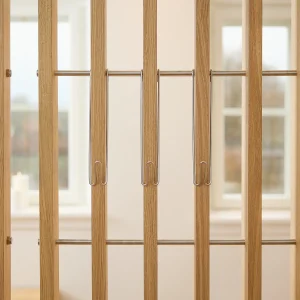 Close-up van een WoodUpp traphekje met slanke eikenhouten verticale spijlen met warme lichte houtkleur en gladde afwerking, en roestvrijstalen horizontale verbindingsstangen; aan drie spijlen hangen WoodUpp metalen veiligheidsclips/haakjes — slanke verchroomde U‑vormige kinderslotjes die het hek extra vergrendelen en een strakke, minimalistische uitstraling geven.