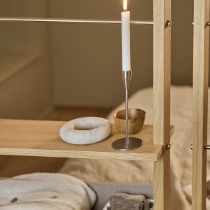 WoodUpp eiken roomdivider met dunne verticale stijlen, metalen stangen en open planken waarop een slanke roestvrijstalen kandelaar met brandende witte dinerkaars, een klein houten schaaltje en een ronde marmeren decoratieve ring staan, sfeervol gestyled en functioneel in neutrale, warme tinten.