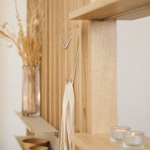 WoodUpp slatwall van licht eikenhout met verticale latten, voorzien van twee chroomkleurige wandhaken en zwevende metalen plankjes. Haken dragen een katoenen doek; planken tonen houten schaaltjes, glazen vaas met droogbloemen en kleine theelichtjes. Functioneel en minimalistisch wandopbergconcept van WoodUpp, stijlvol.