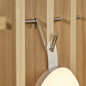 WoodUpp houten lamellenpaneel in licht eiken met verticale groeven, voorzien van een slanke roestvrijstalen haak van WoodUpp. De haak steekt functioneel uit en draagt een rond, lichtgekleurd object aan een kunststof lus, waarbij het minimalistische ontwerp en de nette afwerking opvallen.