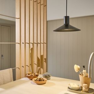 WoodUpp lattenwand als roomdivider van licht eiken met geïntegreerde metalen stangen en haken van het WoodUpp-systeem, waar een gestreepte theedoek aan hangt. Op het keukenblad staan houten schaaltjes met paddenstoelen, een glazen potje en een afwasborstel; rustige, minimalistische sfeer met hanglamp.