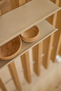 Close-up van WoodUpp-opstelling: lichtgrijs zwevend WoodUpp-plankje met twee ronde, ondiepe houten schaaltjes op een WoodUpp eiken lattenwand. De schaaltjes tonen golvende houtnerf en warme tinten; het smalle, minimalistische plankje heeft afgeronde randen en een matte afwerking, met rustige, sfeervolle uitstraling.