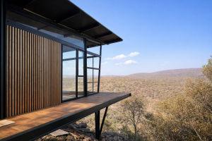 Een modern architectonisch gebouw op een klif met een weids uitzicht over de natuur. De gevel is prominent bekleed met verticale houten latten van WoodUpp, wat zorgt voor een warme, stijlvolle uitstraling naast de stalen kozijnen en het houten terras.